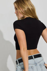 Woman wearing a black crop top and light blue jeans against a plain background